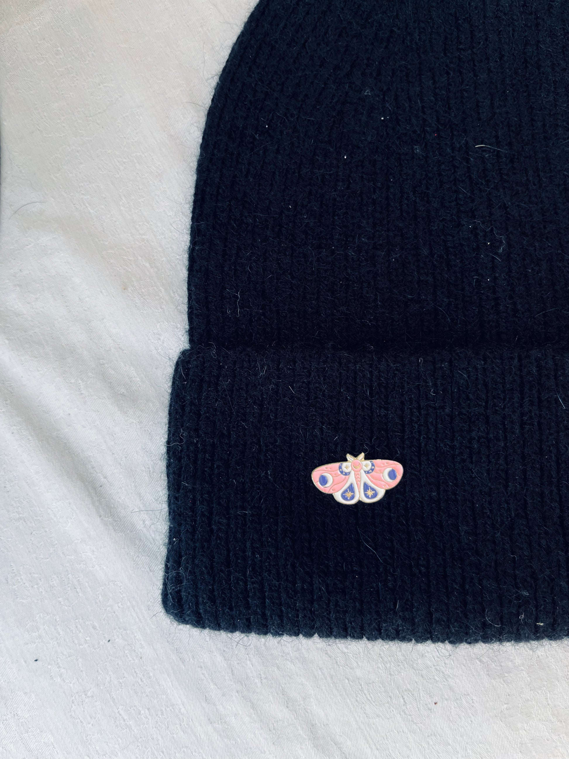 Black knit angora beanie with a pink butterfly pin on a side