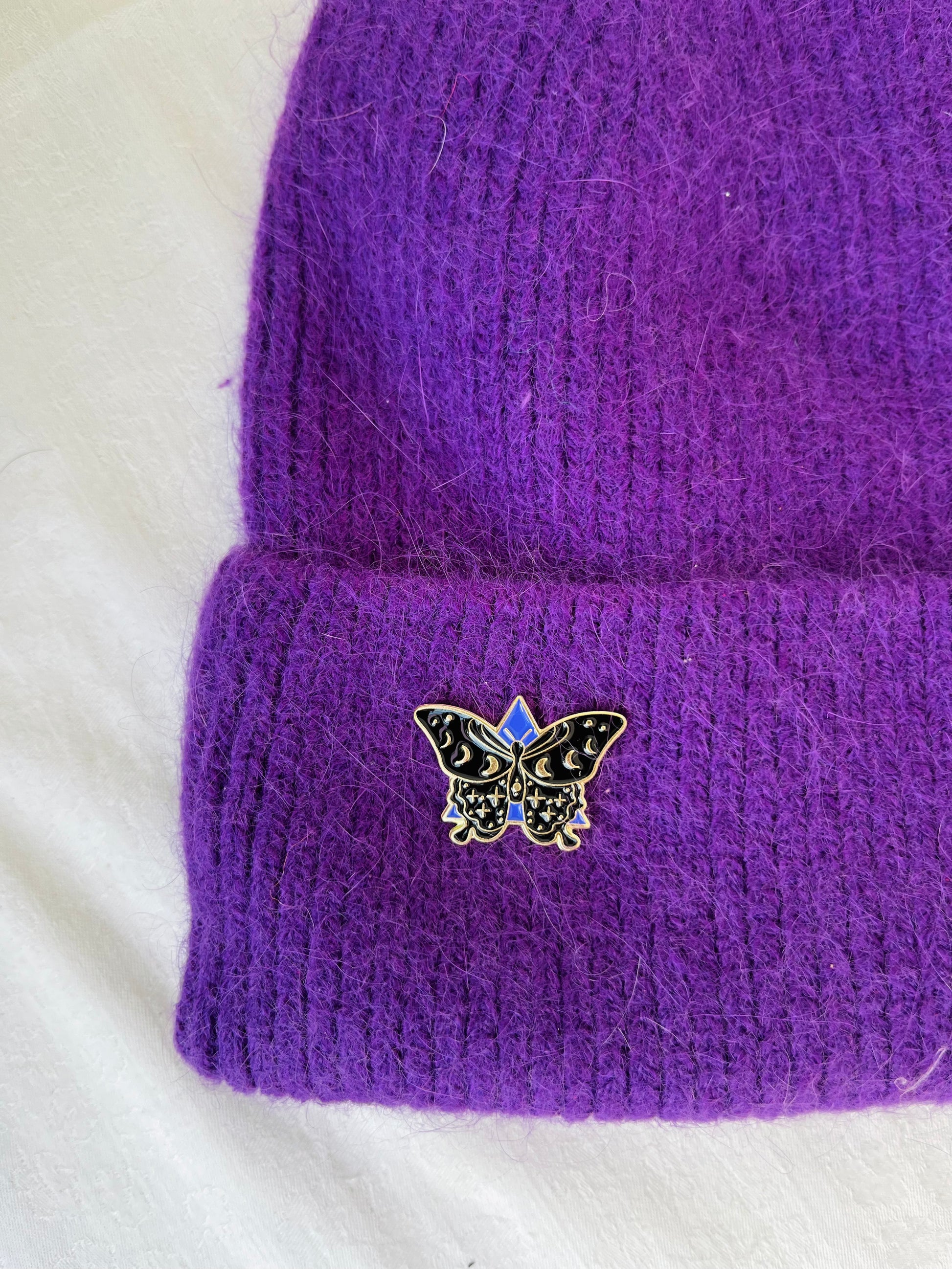 Purple knitted angora beanie or hat with a butterfly pin on a white background