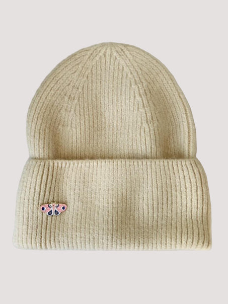 Beige knit angora beanie in a creamy color with a small decorative butterfly brooch on a white background